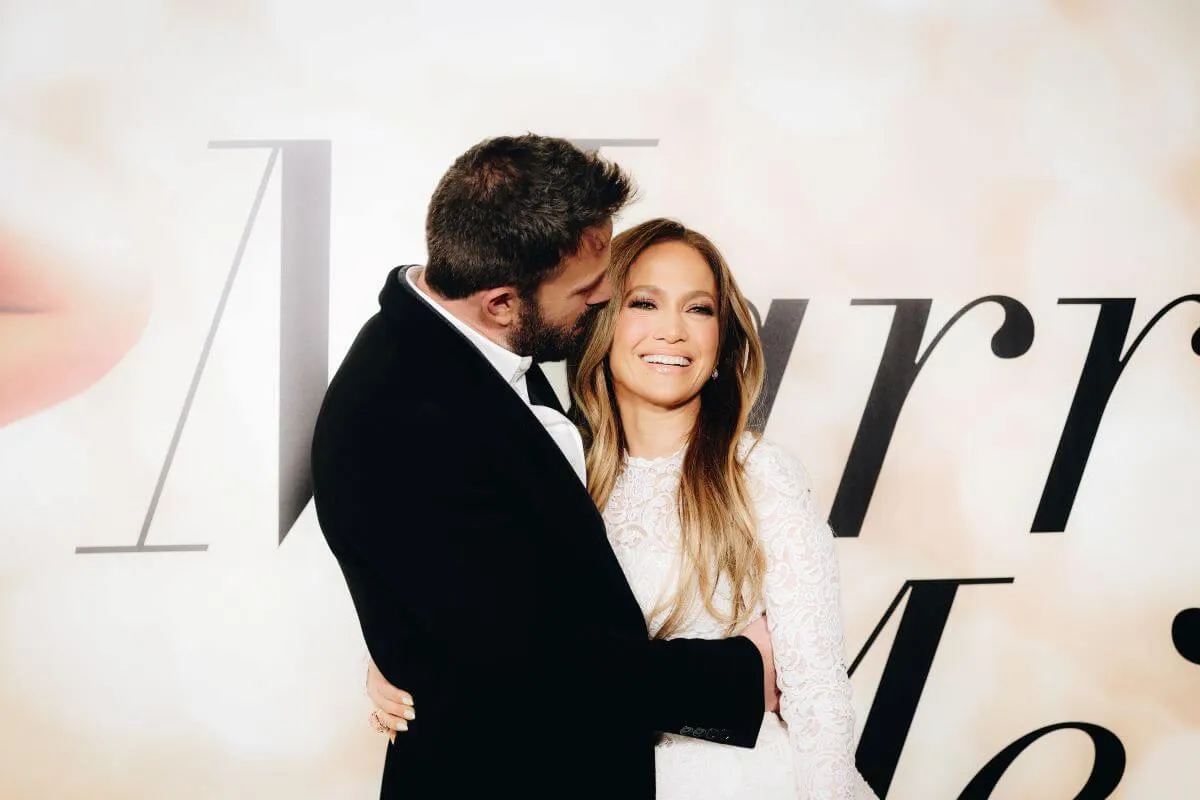 Ben Affleck and Jennifer Lopez stand in front of a sign for her film 'Marry Me.' He embraces her.