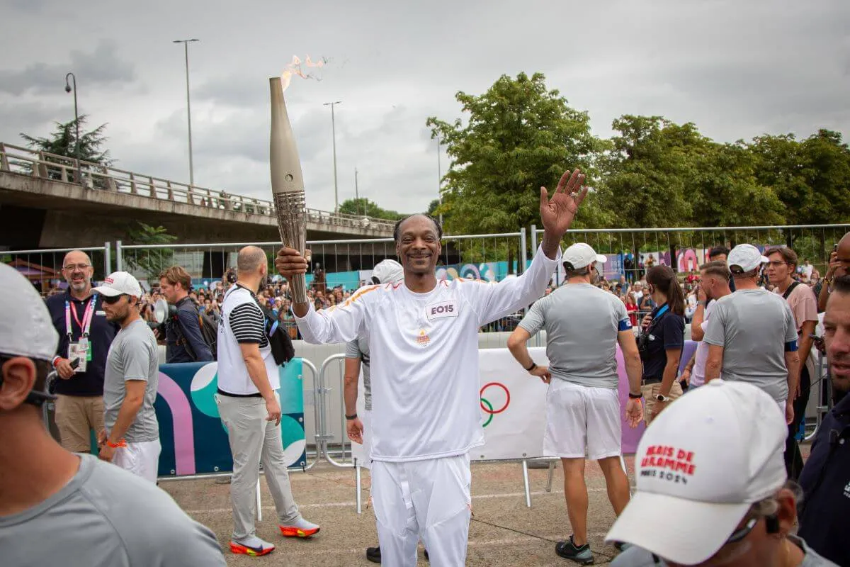 Snoop Dogg wears a white outfit and holds the Olympic torch.